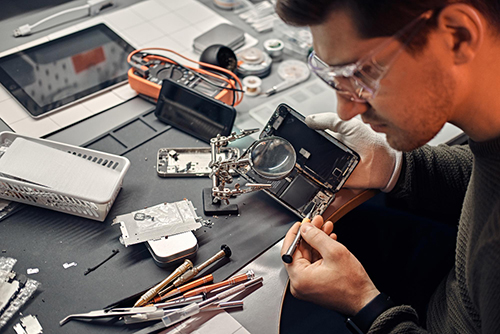serviceman uses magnifier screwdriver repair damaged smartphone electronic workshop